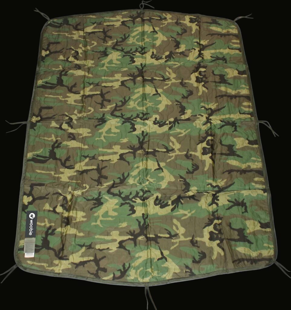Camouflage-patterned fabric sheet with tie-down cords at the edges, laid flat on a dark background.